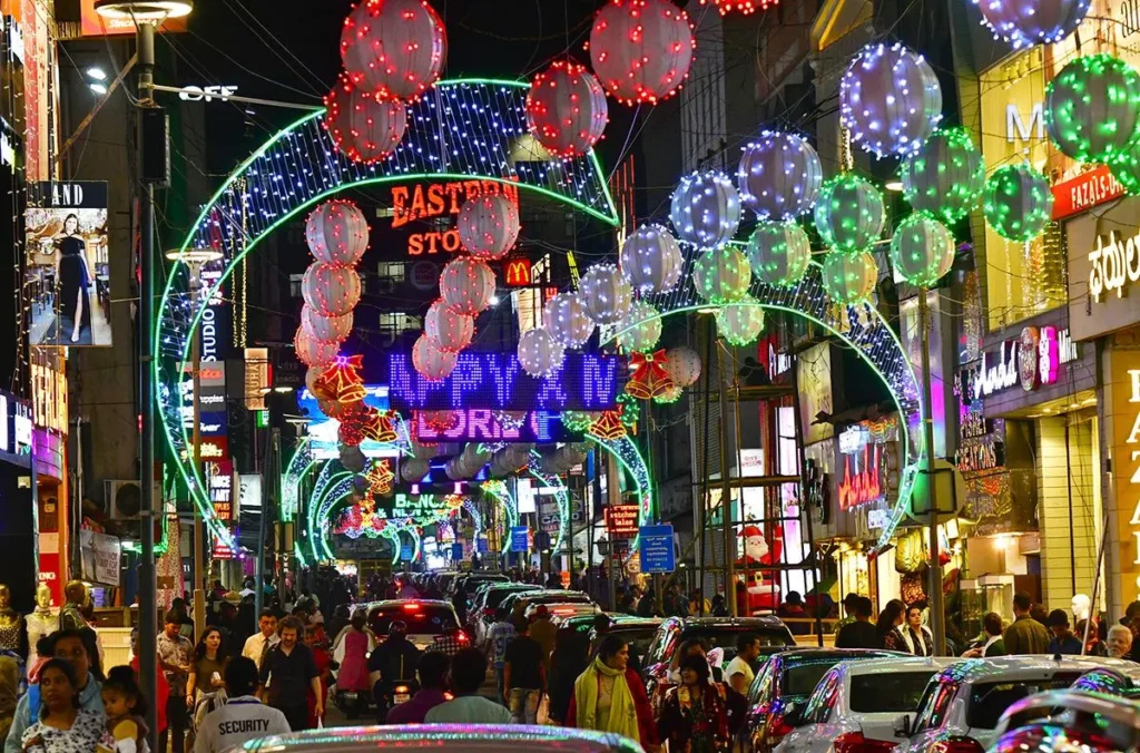 well lit church street in bangalore with fairy lights and christmas lanterns. Crowd of people and cars on the street , stores on each side